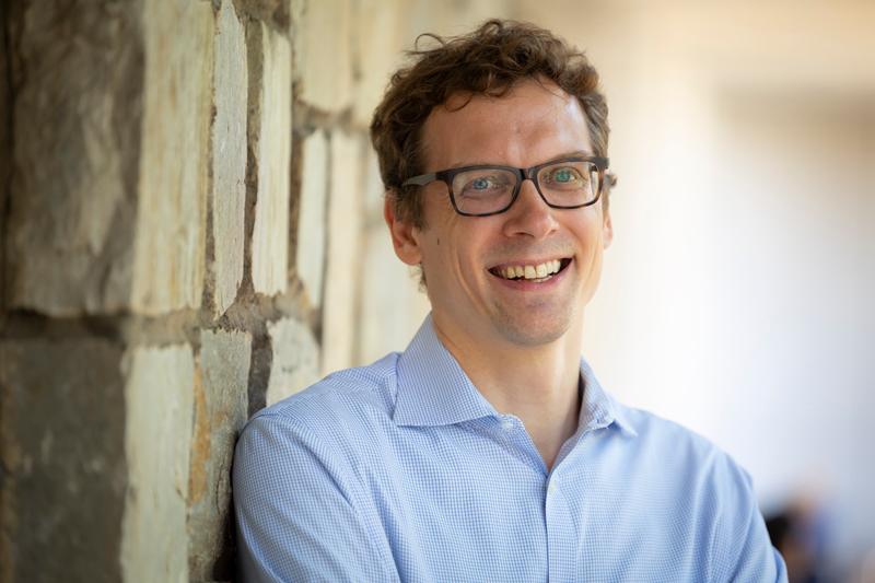 man smiling wearing glasses leaning against wall outdoors