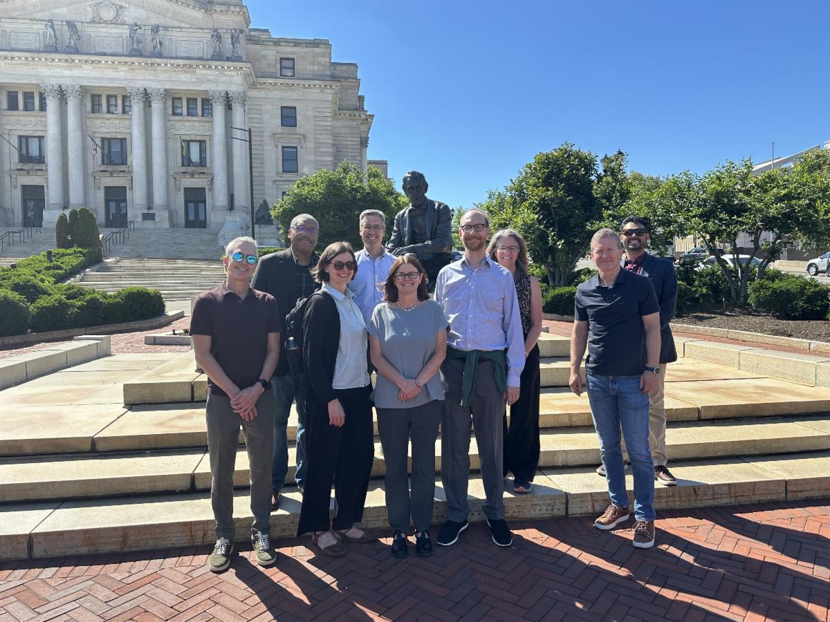 group of people standing on steps in front of large building smiling on sunny day 