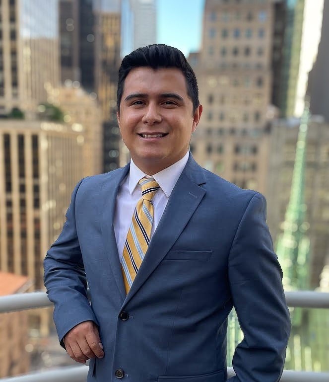 man smiling in blue suit leaning on rail with cityscape behind him