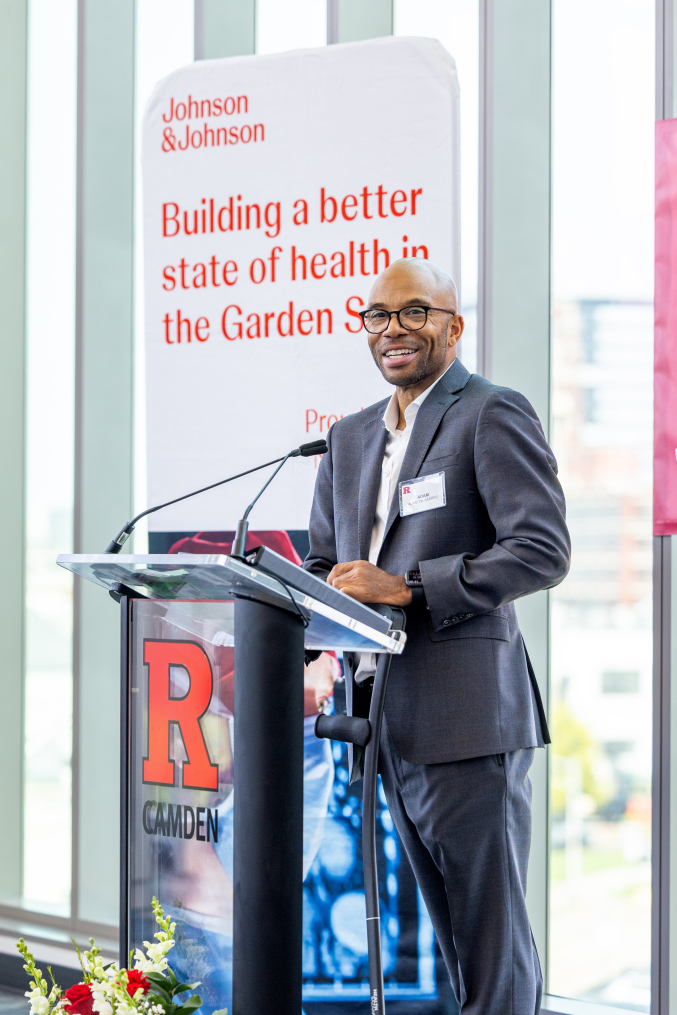 man wearing business suit standing at lectern with R Camden logo on it