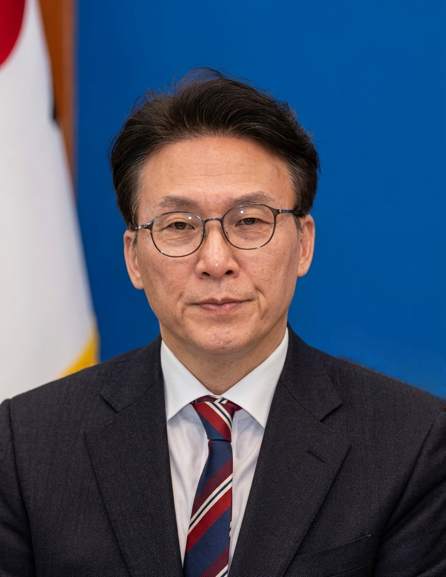 man in business suit looking forward in front of blue background and an unidentifiable flag in the back left side