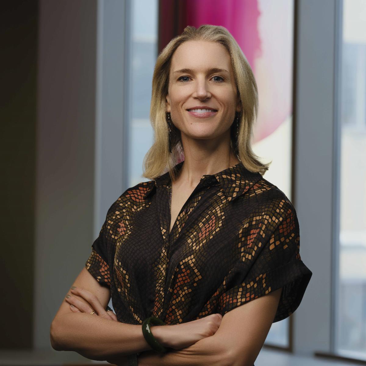 woman with printed blouse and arms folded smiling in front of window