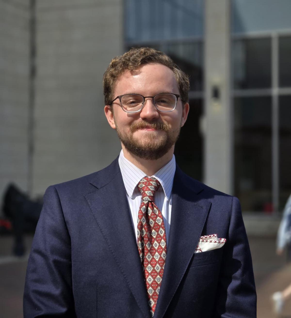 man in business suit smiling outdoors in front of building