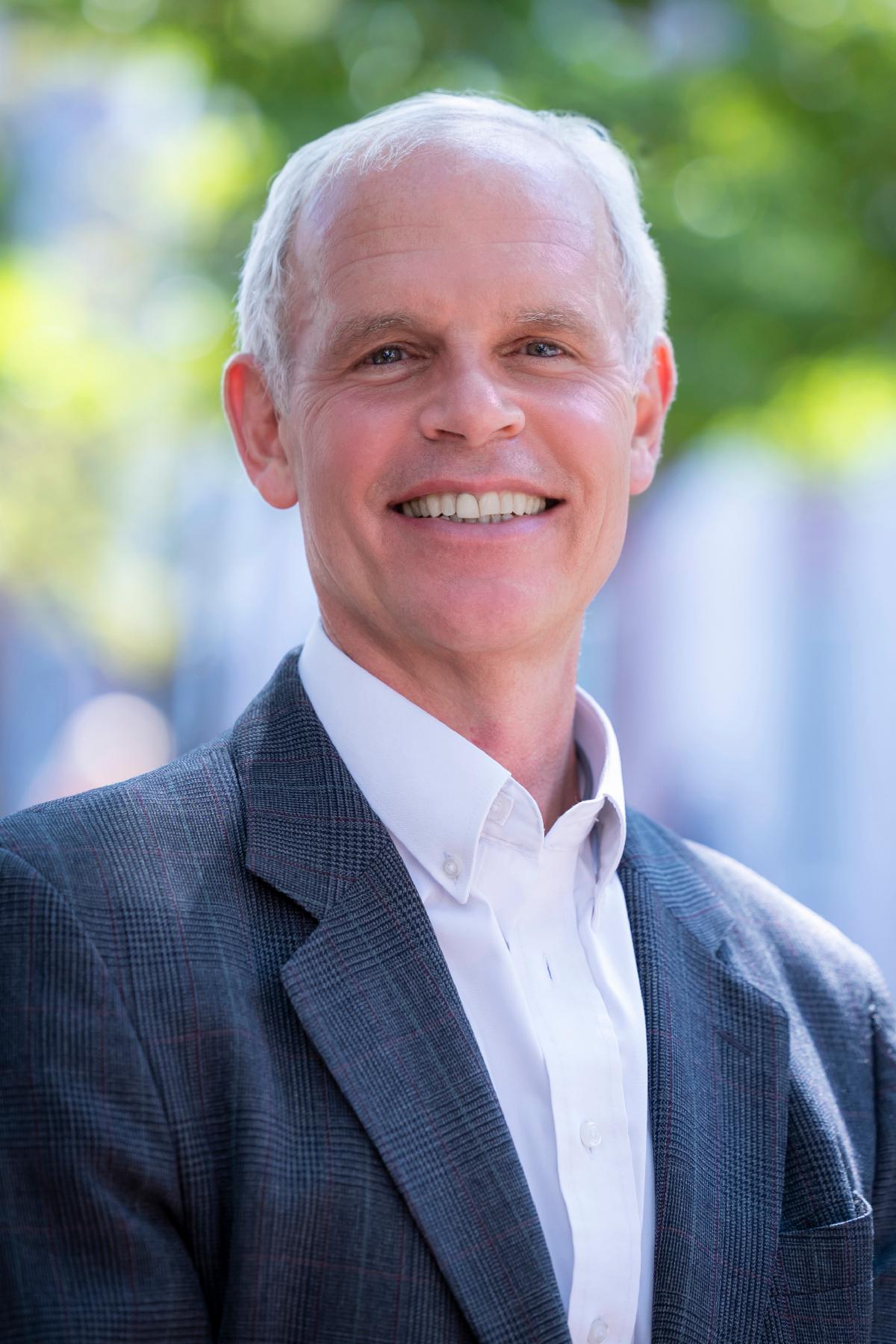 man in blazer and shirt smiling outdoors