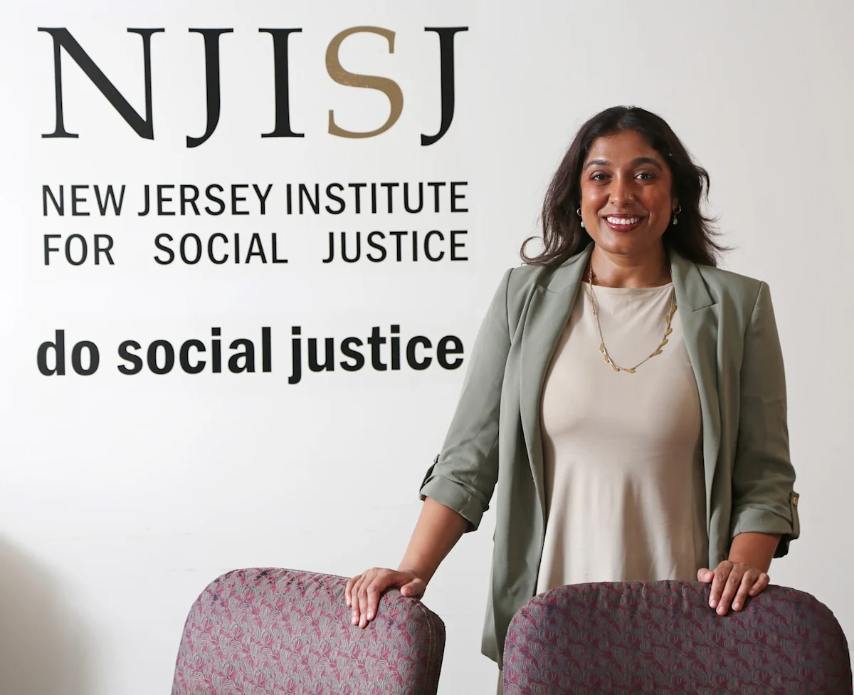 woman smiling holding the backs of two chairs in white walled room with text on the left side of image