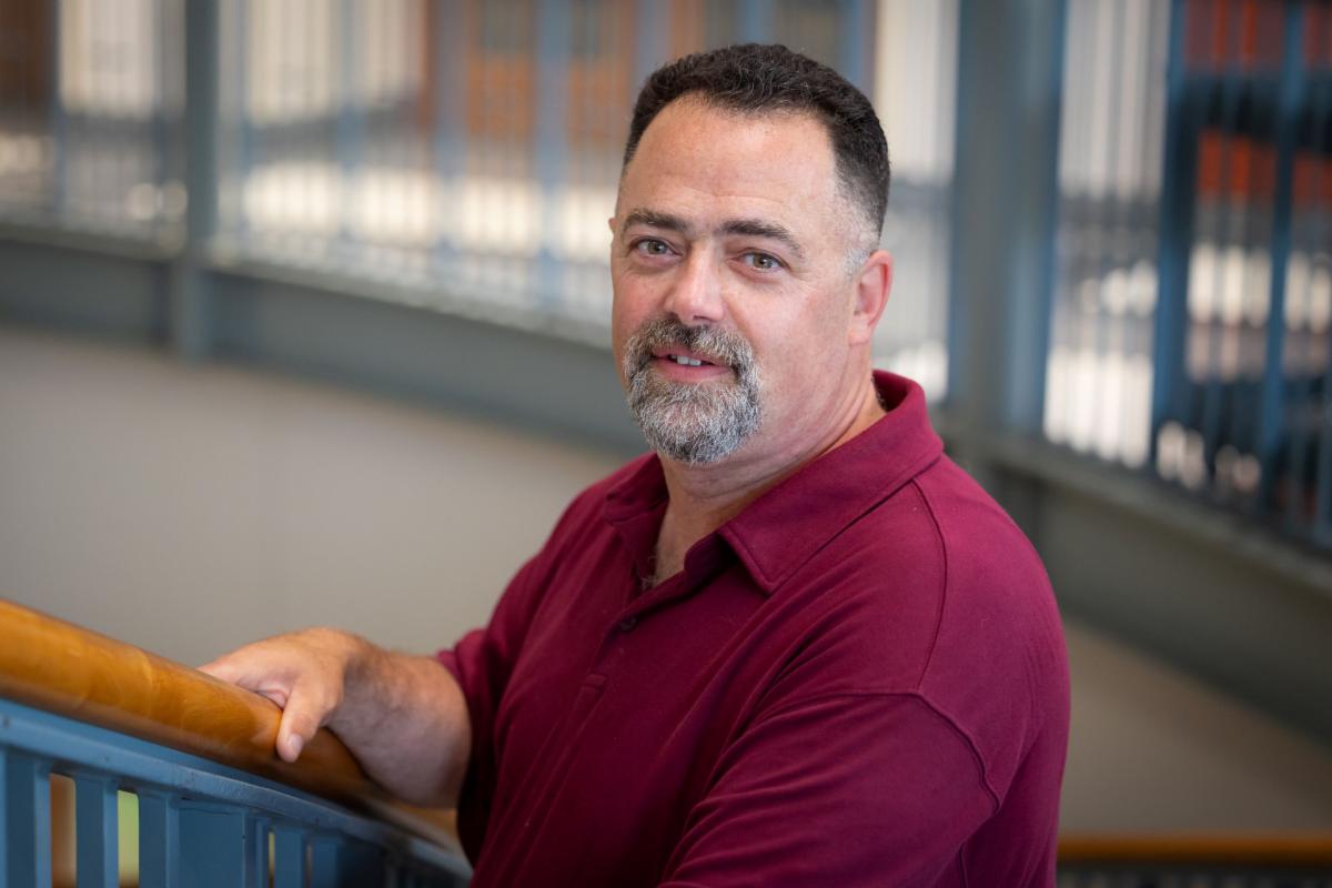 man in maroon polo smiling and leaning on stair railing