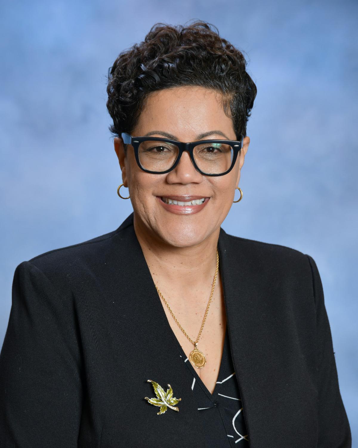 woman wearing dark suit and glasses smiling in front of blue background