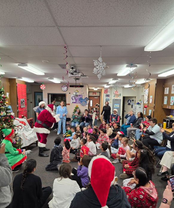 Davila students and staff gathered in a decorated classroom visiting with Santa
