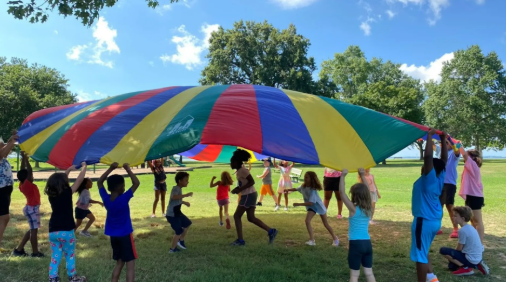 Kids playing together at a summer camp under a colorful parachute