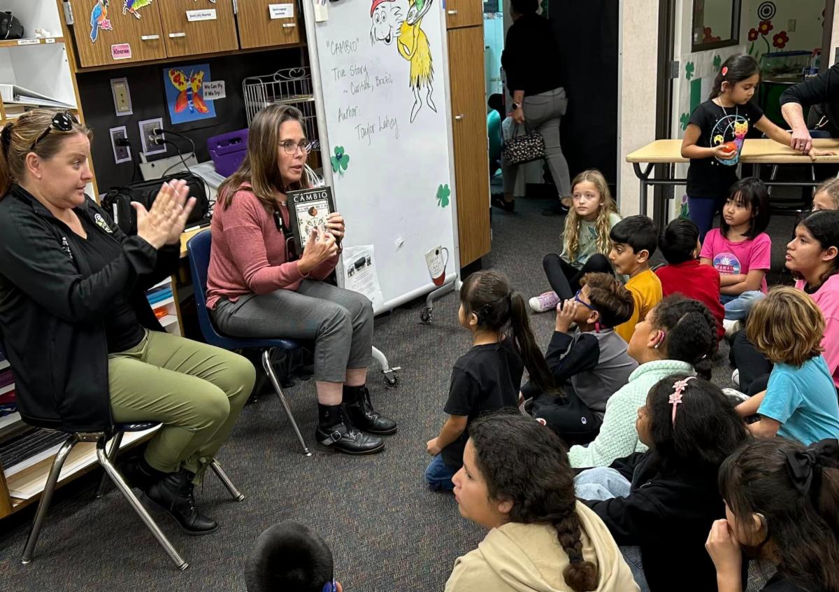 Staff holding a book and students sitting on carpet looking at book being read.
