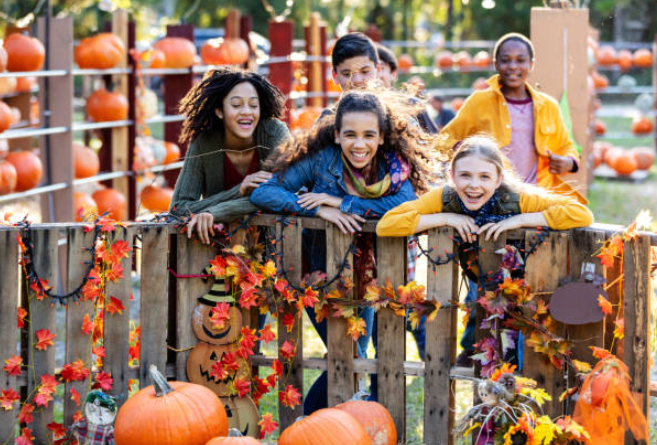 children smiling together posing at a decorated fence with fall trees and leaves