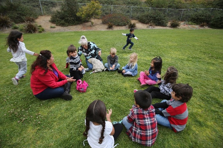 Image of children and teacher sitting outside on grass