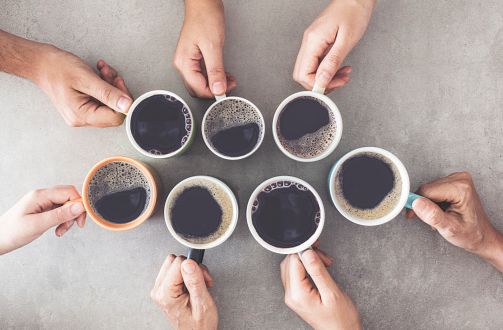 Group of coffee cups being held by hands around a table