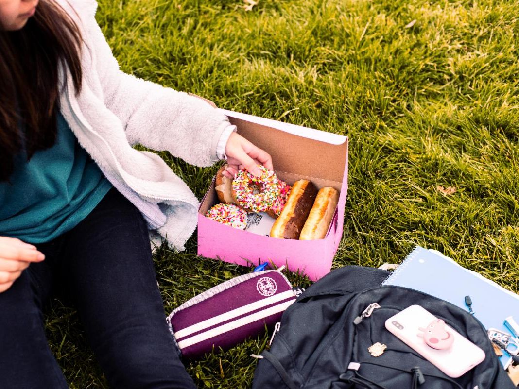A woman grabbing a donut from a box.