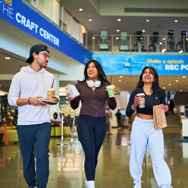 Three people walking and laughing with drinks and food in their hands