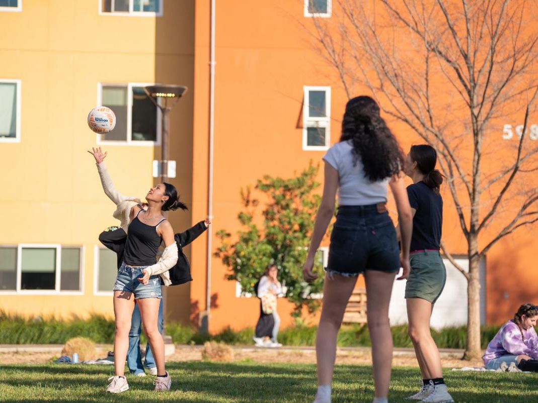 Three women playing volleyball on a lawn.