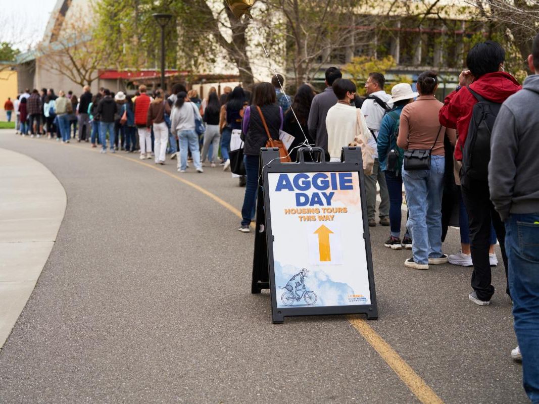 A line of people with a sign that says Aggie Day Housing Tours This Way.