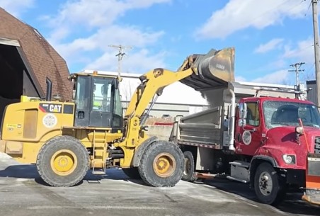 loader dumping salt into red plow truck