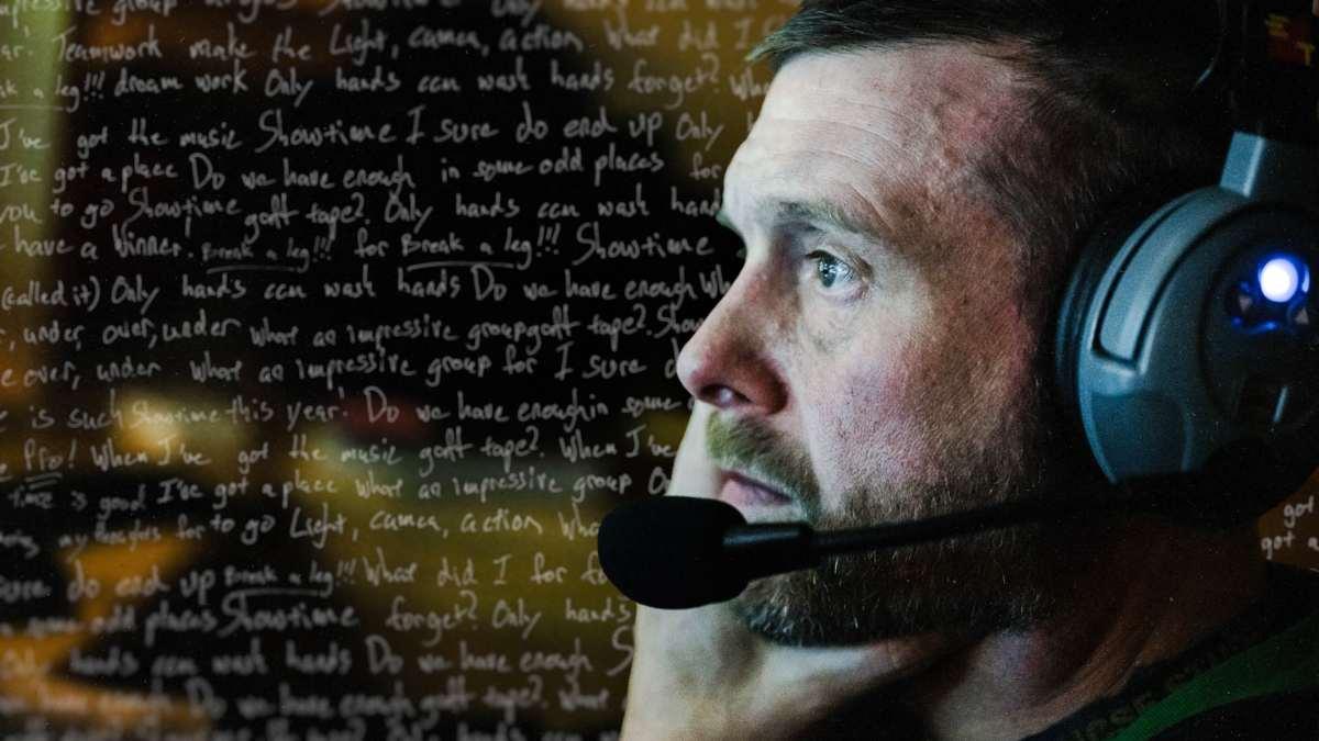 Man with headset looks into bright screen with written text in background.