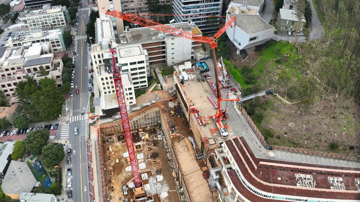 Two red cranes hover over construction site.