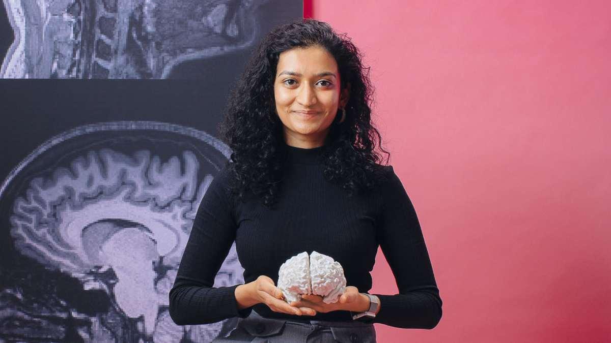 Smiling woman holds brain sculpture with a two colored split background.