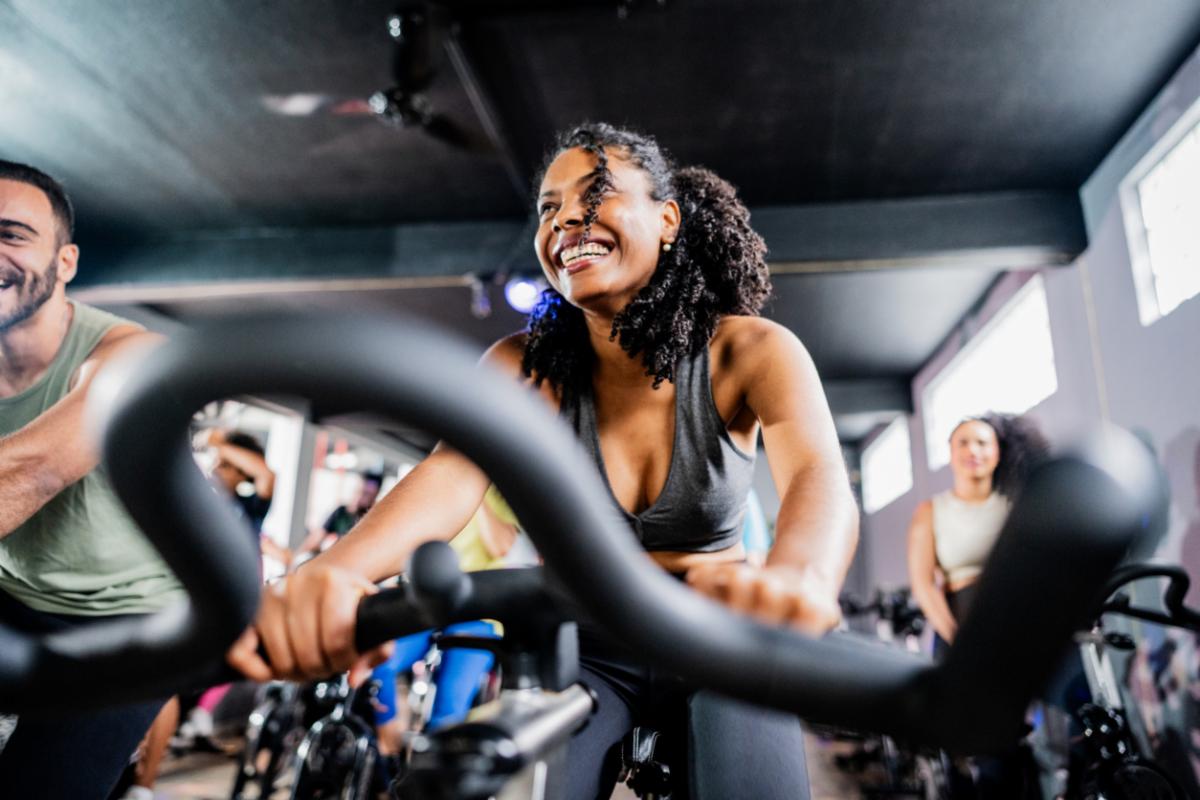Smiling woman rides a stationary bike during a group cycling class at a fitness center.