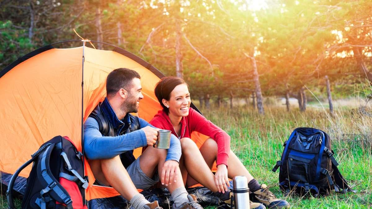 Two young smiling people sitting outside of a tent at sunset.