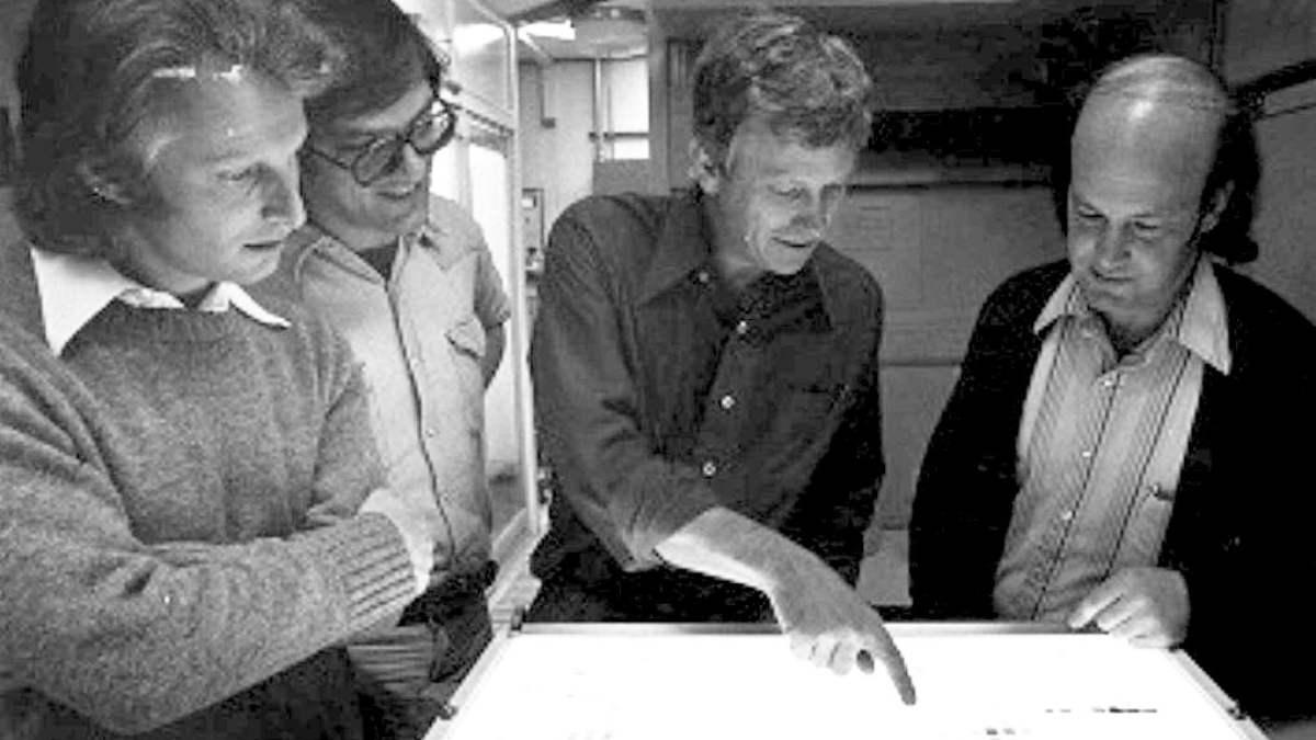 Group of scientists point at light box in dark room.