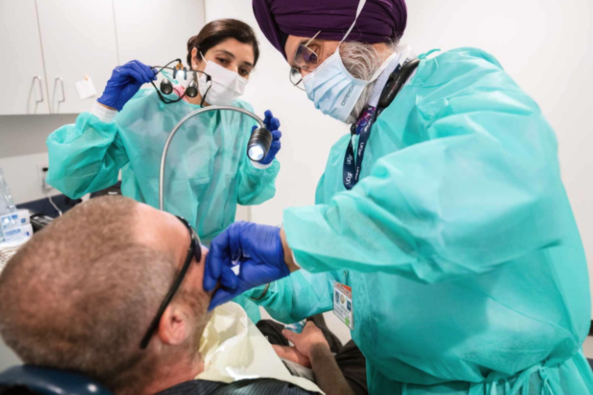 Two UCSF health care providers wearing protective equipment examine a patient during a dental procedure.