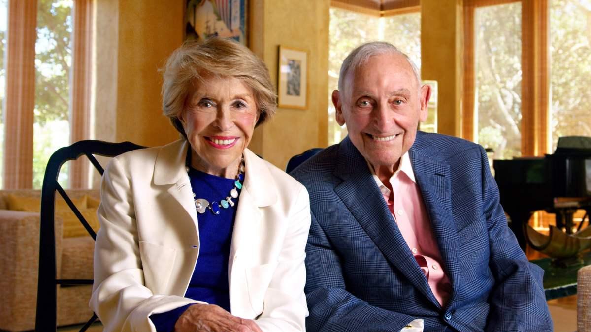 A well-dressed older couple smiles.