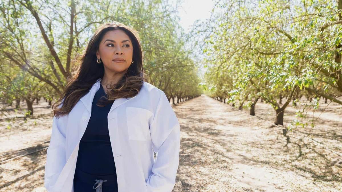 Woman wearing a lab coat standing in an orchard