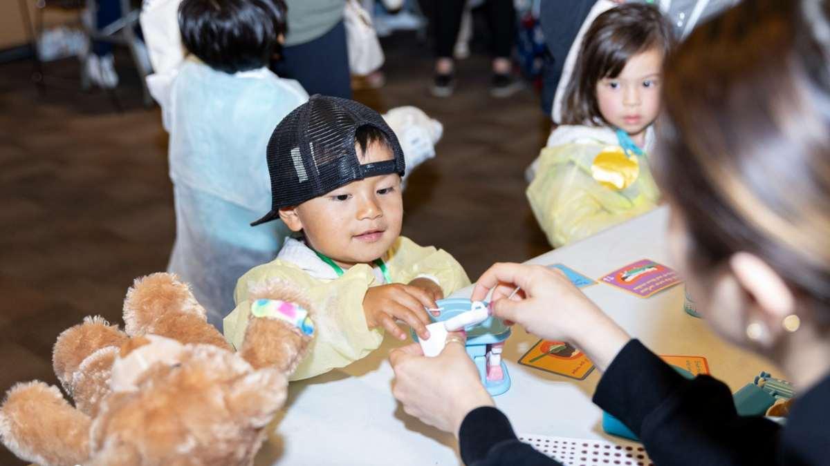 Toddler with hat backwards looks up at table to receive an object.