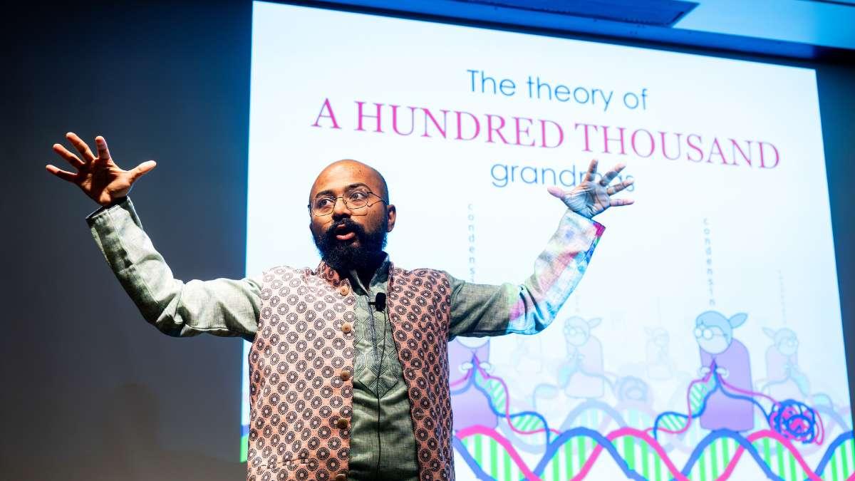 Enthusiastic speaker uses hands to present with colorful projection on face.