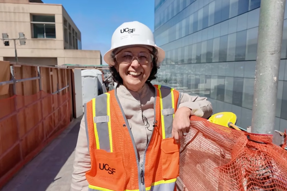 Smiling UCSF staff member wearing a hard hat and orange safety vest at a construction site.
