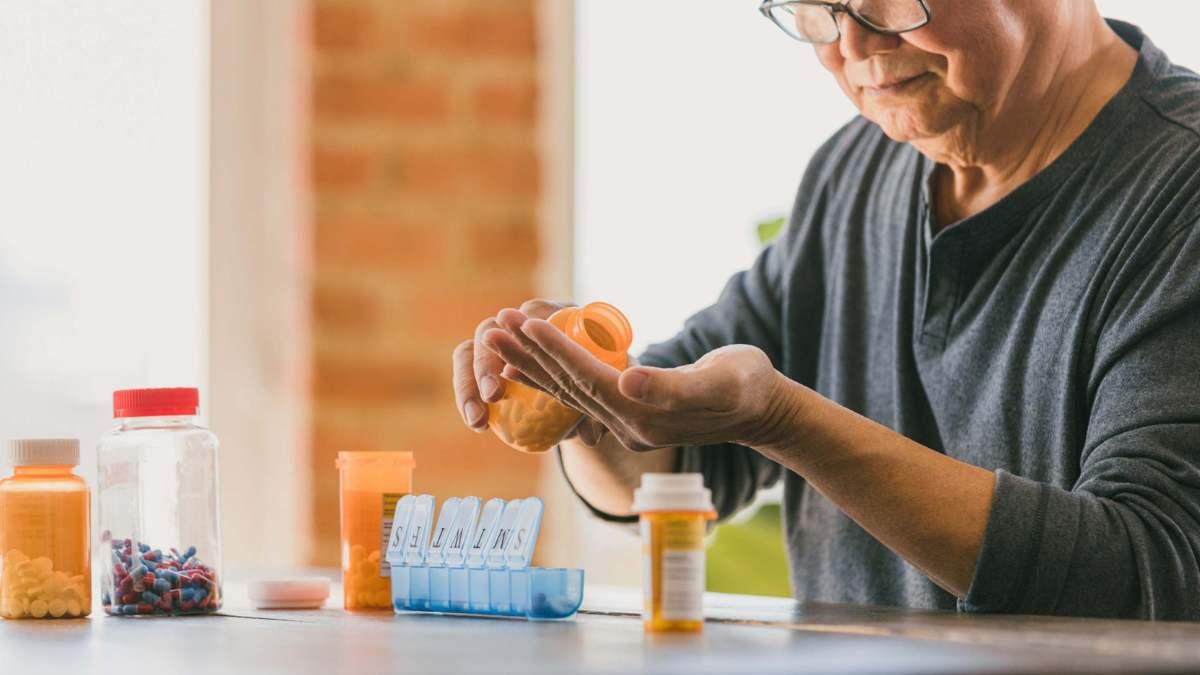 Man pouring pills into his hand next to medication bottles