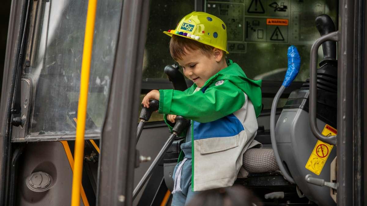 Little boy wearing a construction cap pushes the levers of a school bus.