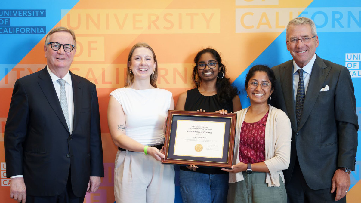 Five people pose with a framed University of California student leadership award, smiling before a UC-branded backdrop.