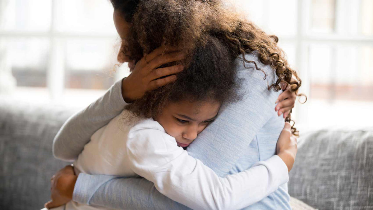 A mother holds her young daughter who shows signs of stress.