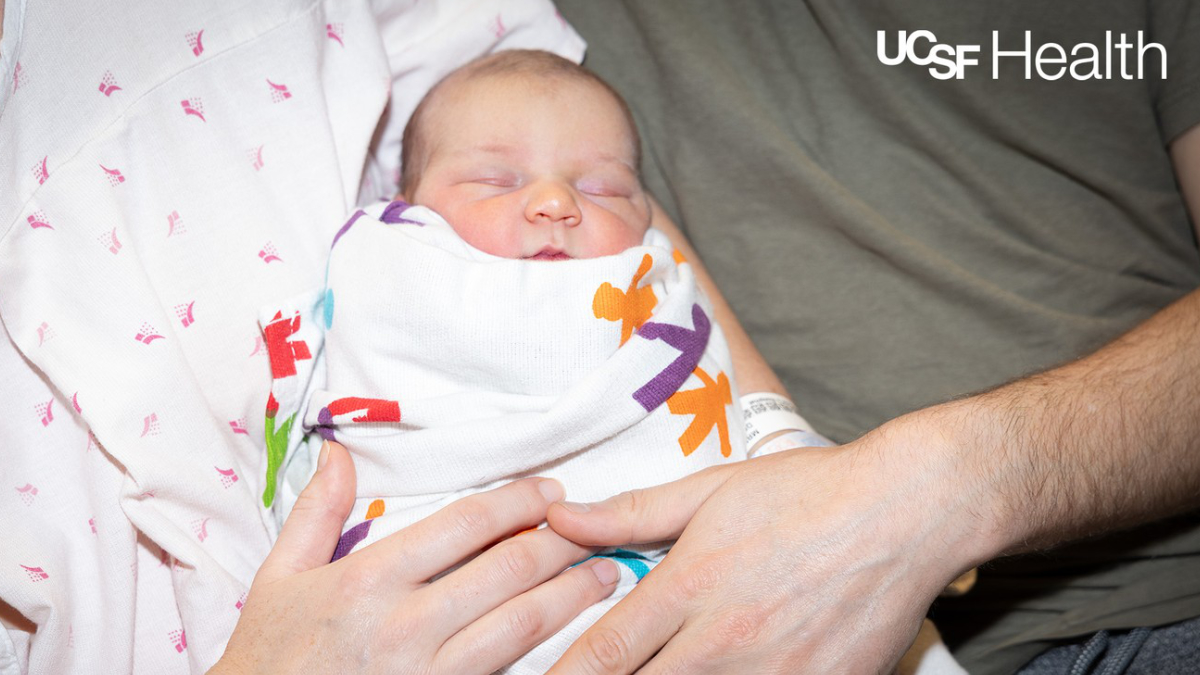 A swaddled newborn held by two parents.