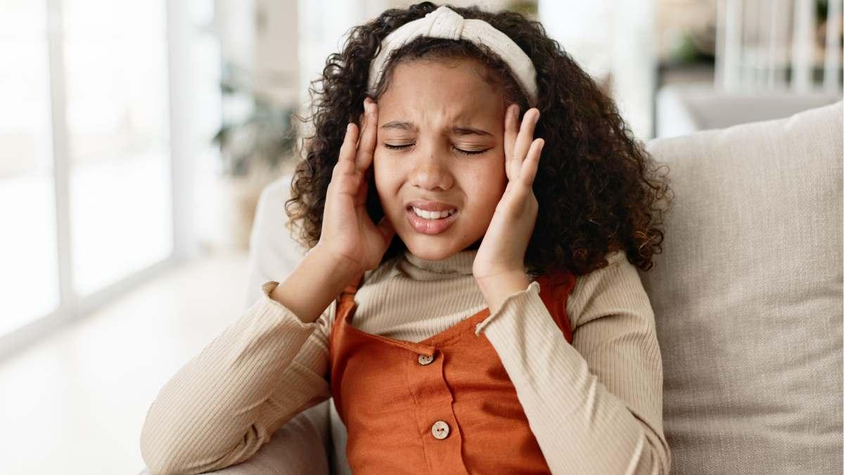 Young girl holds her head in pain.
