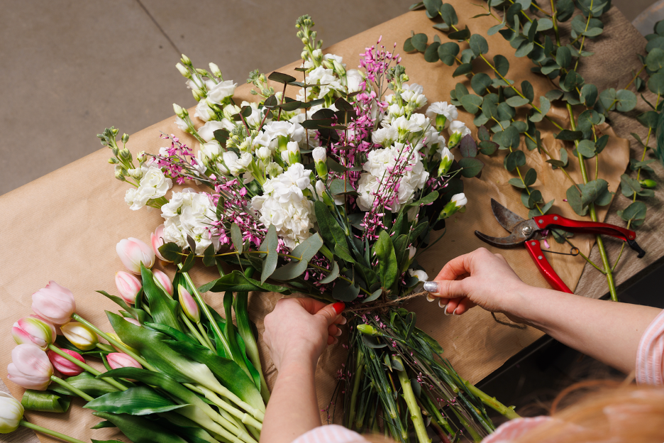 White and pink cut flowers and foliage being arranged and tied with twine, making a bouquet  