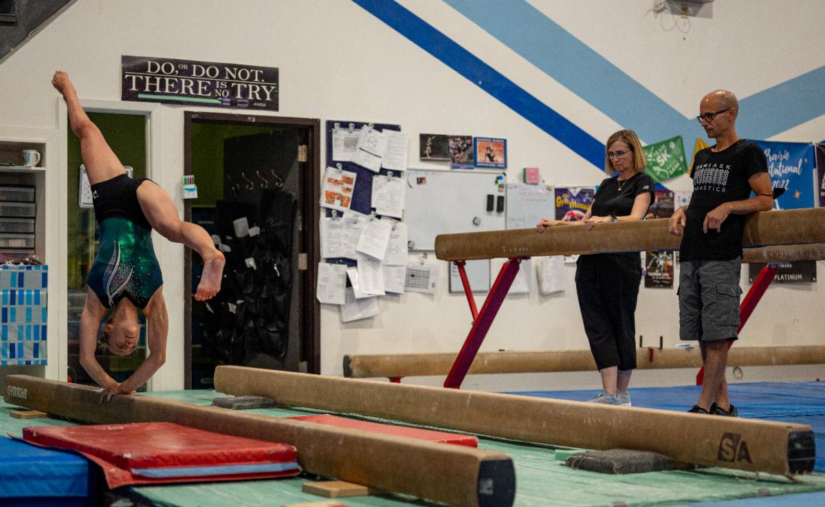 Gymnastic coaches Dana Brass and Chris Baraniuk watch an athlete as she practices on the beam.