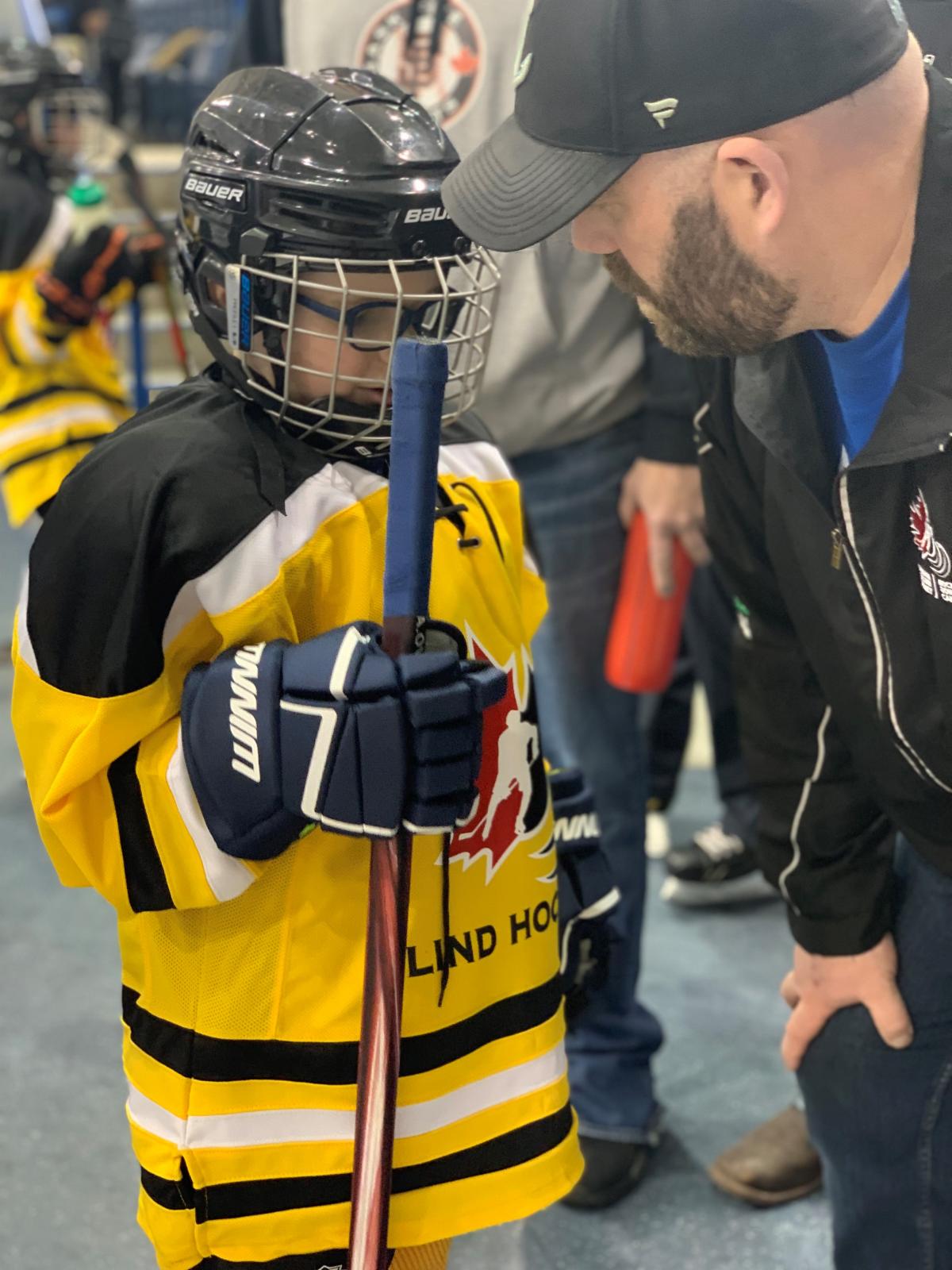 A photo of blind hockey player Isaiah Gauthier receiving instructions