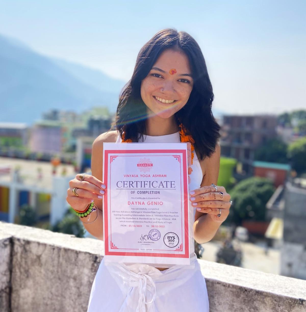 Dayna Genio, BeHERE Scholar, in a white dress holding up a certificate