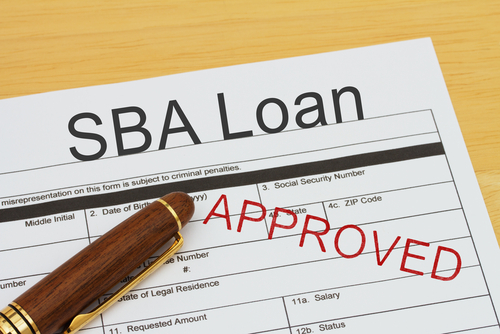 Applying for a SBA Loan Approved_ SBA Loan application form with a pen on a desk with an approved stamp
