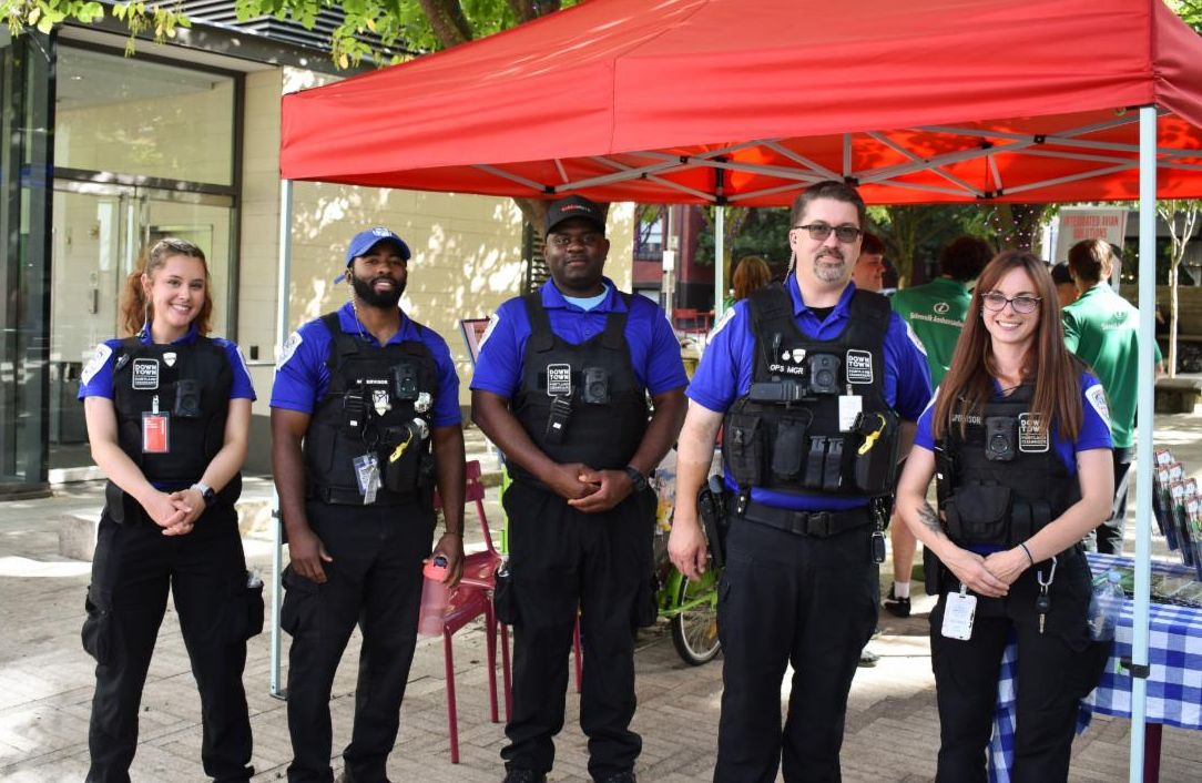 image of give people standing together dressed in security uniforms smiling in front of a red tent