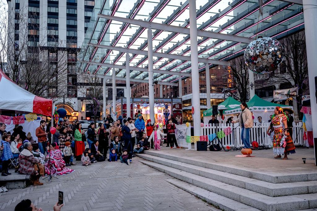 Collection of people attending a cultural event at Director Park in Downtown Portland. Two performers are seen on stage.