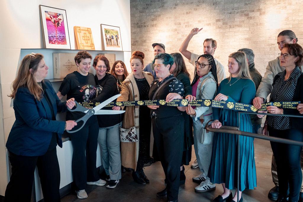 image of a group of people together holding a ribbon with someone on the end holding oversized scissors about to cut the ribbon