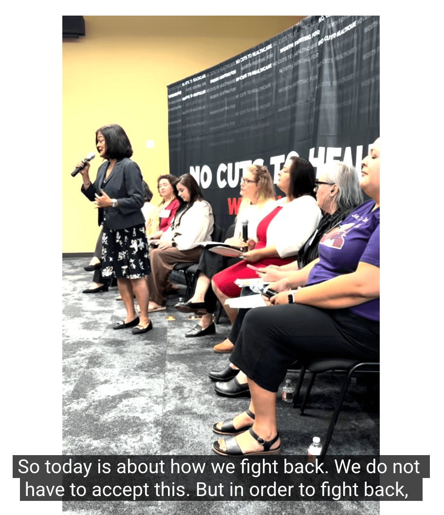 Rep. Jayapal stands and speaks into a mic, with a row of adult speakers seated behind her