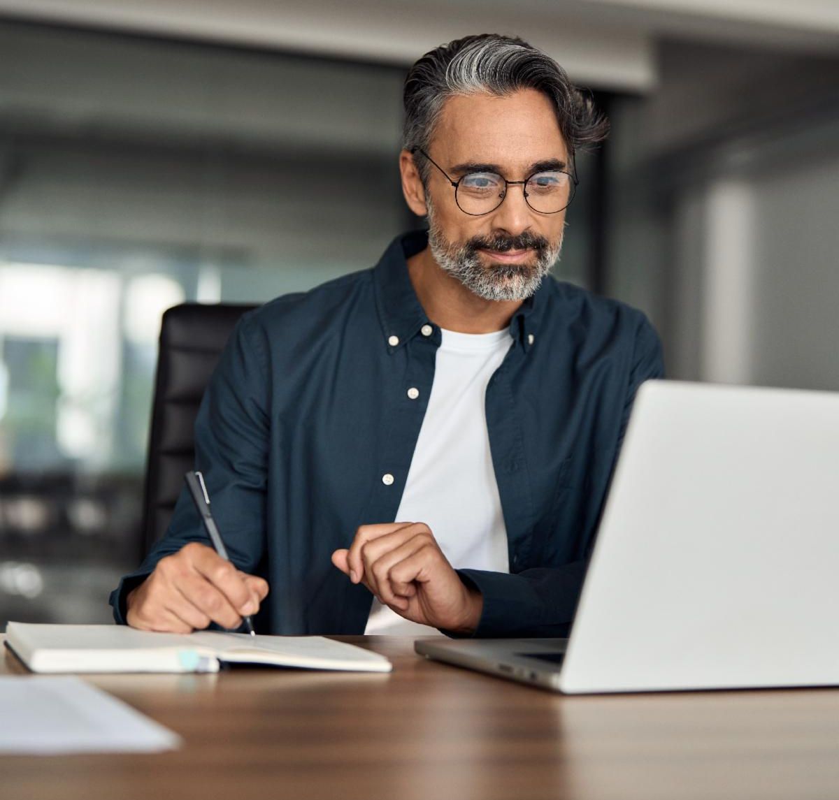 A man takes notes while watching a webinar.